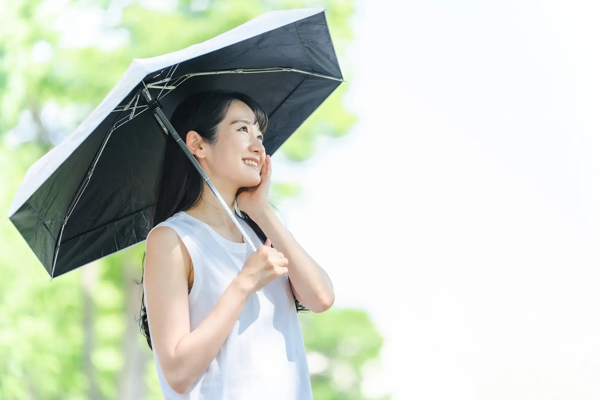 紫外線対策をする女性。黒い日傘を差している