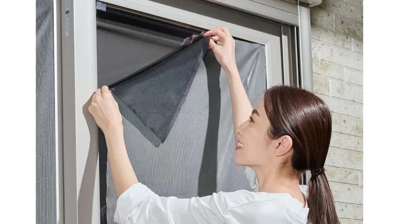 屋外から商品『太陽熱カット』を窓に貼り付けている女性。