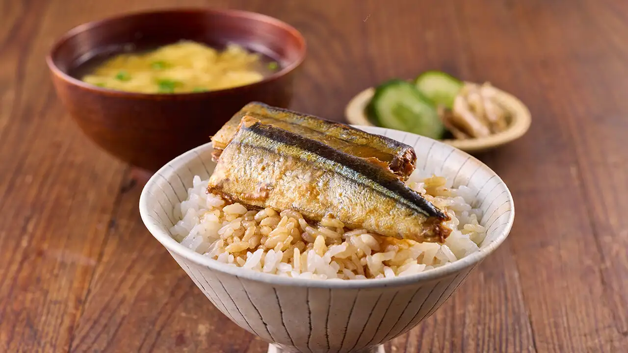 茶碗に盛った白米に煮魚を汁ごと乗せた様子。奥に味噌汁と漬物も置かれている。