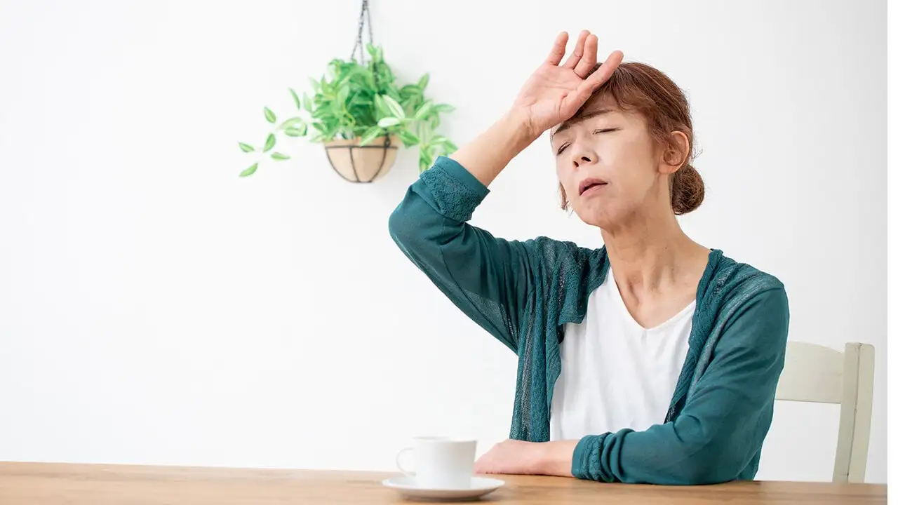 室内で椅子に座り頭に手を当てる女性