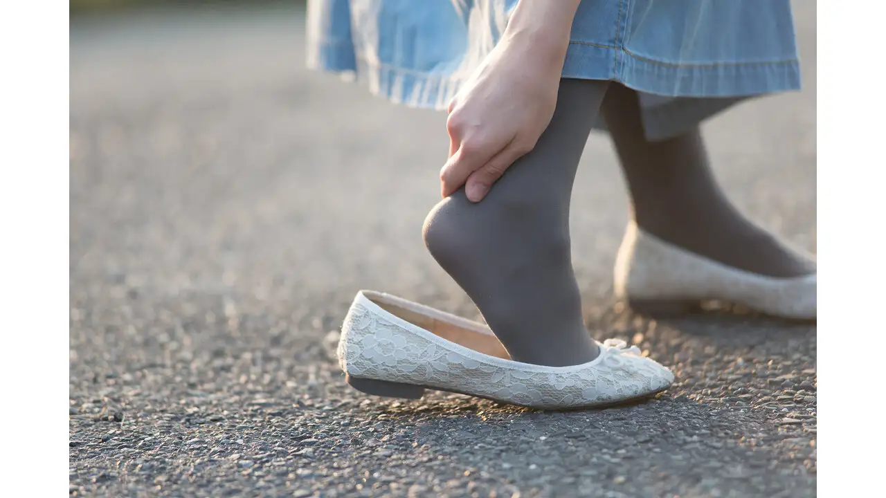 白いレースのパンプス、グレーのタイツをはき、かかと側の靴ずれを気にしている女性