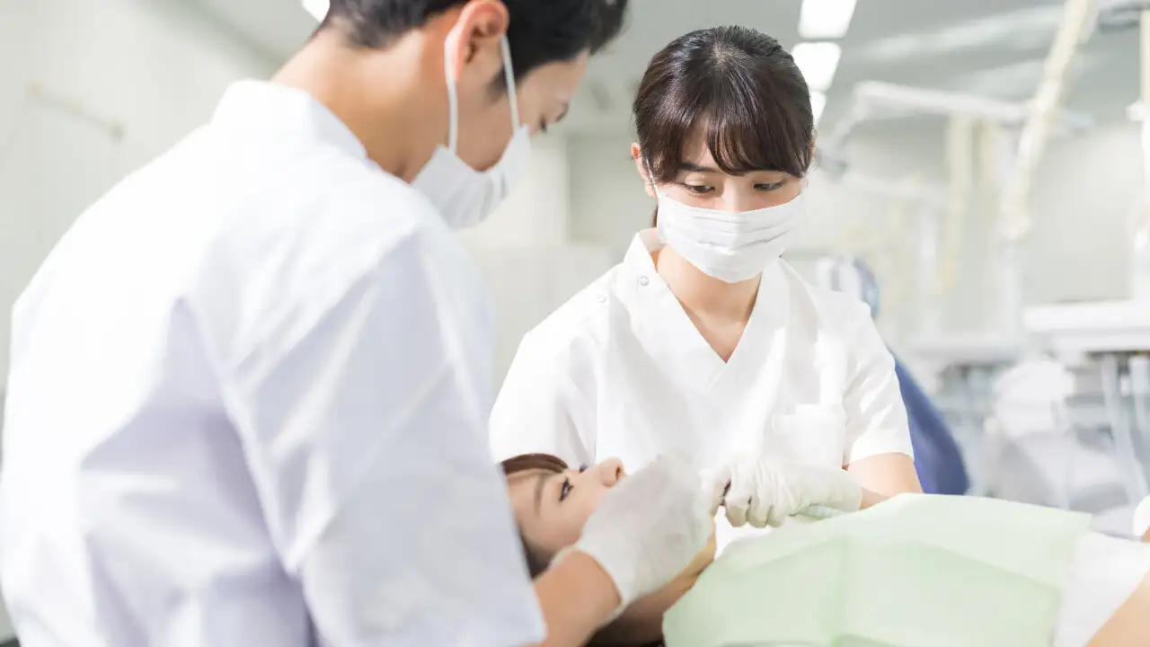 歯科で健診を受けている患者と、医療器具を手にした歯科医2人