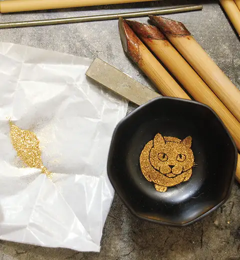 漆で絵を描いた上から、粉筒(写真右)で金粉を蒔き付けて乾かす イメージ
